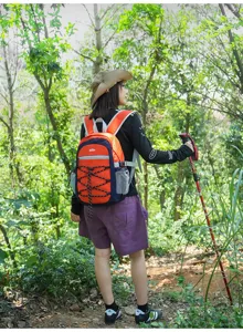Rückansicht einer Wanderin mit orange-blauem Rucksack, elastischer Schnürung und Seitentasche im Wald