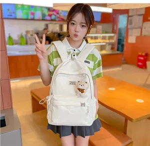 Modèle portant un sac à dos crème avec poche avant et petit ours en peluche accroché