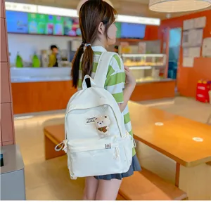 Vue de dos d’une élève portant un sac à dos blanc avec un petit ourson dans un café lumineux