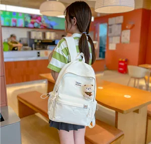 Vue de dos d’une élève portant un sac blanc avec breloque ours en peluche dans un café