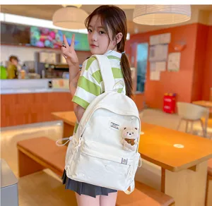 Une élève porte un sac à dos blanc avec poche avant zippée et porte-clés ourson dans un café