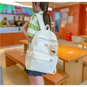 Dans un café, une personne porte un sac à dos blanc avec poche zippée et breloque ourson