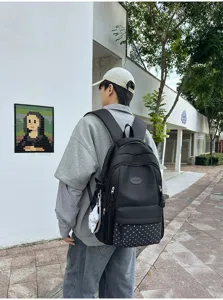 Vue arrière d’un sac à dos noir avec poche avant à pois et breloque, porté en extérieur