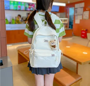 Vue de dos d’une élève portant un sac à dos crème avec un petit ours dans un café chaleureux