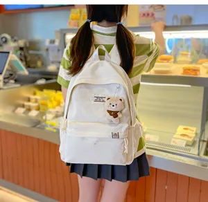 Vue de dos d’une élève portant un sac à dos blanc avec poche zippée et petit porte-clés ours