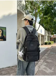 Vue de dos d’un sac à dos noir porté dehors, avec motif étoilé en bas et breloque étoile blanche