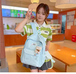 Une élève porte un sac à dos bleu clair à poches avant, avec un petit ours en peluche, dans un café
