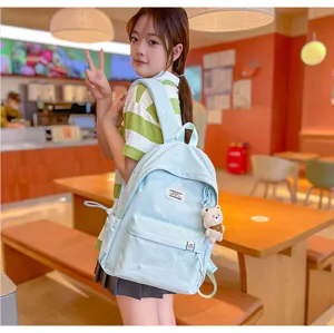 Sac à dos bleu clair aux étoiles brodées, avec pendentif ourson, porté par un modèle en intérieur