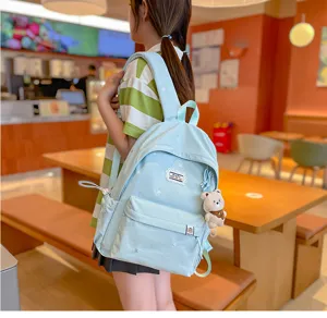 Dans un café, une élève porte un sac à dos bleu clair brodé avec un pendentif ours en peluche