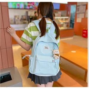 Vue arrière d’une élève portant un sac bleu clair avec broderies étoilées et un pendentif ourson