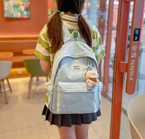 Vue de dos d’une élève avec sac à dos bleu clair, poche avant et ours en peluche dans un café