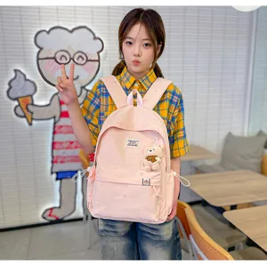 Une élève porte un sac à dos rose avec un pendentif ours en peluche, dans un intérieur lumineux