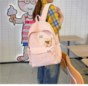 Une personne porte en intérieur un sac à dos rose pâle brodé d’étoiles, avec un petit ourson