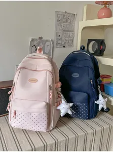 Deux sacs à dos rose et bleu marine, avec imprimé étoiles et breloques, sur une table rayée.