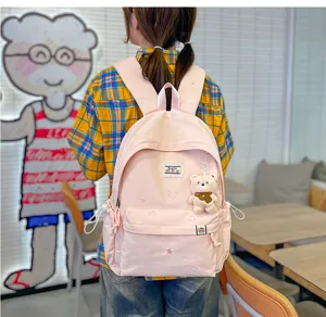 Vue de dos d’une élève portant un sac rose pâle, brodé d’étoiles, avec un petit ours en peluche