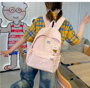 Vue de dos d’une élève portant un sac à dos rose pâle, brodé d’étoiles et orné d’un ourson suspendu