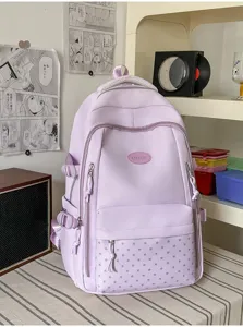 Sac violet clair posé sur un bureau, avec une poche avant à étoiles et plusieurs fermetures éclair