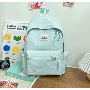 Sac à dos vert menthe pâle avec étoiles brodées et poche avant, posé sur un bureau près de livres