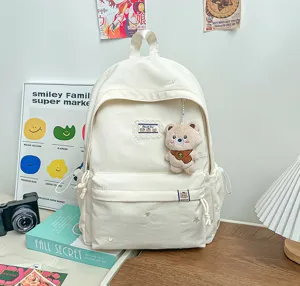 Sac à dos blanc avec broderies, poche avant et petit pendentif ourson, présenté sur une table
