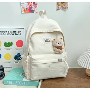 Vue de face d’un sac à dos ivoire avec breloque ourson, écusson brodé et poche zippée