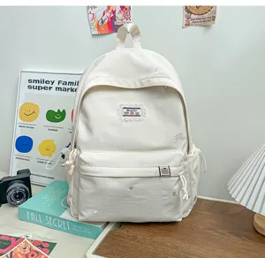 Sac à dos blanc avec petite broderie d’ours, poches avant et latérales, posé sur un bureau