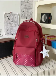 Sac à dos rouge avec poche avant à étoiles et breloque étoile blanche, posé sur un tapis rayé