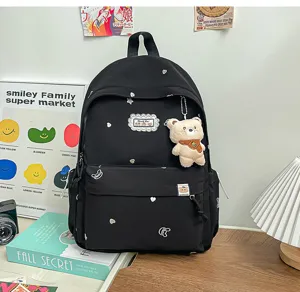 Vue de face d’un sac à dos noir avec des cœurs et étoiles argentés et un pendentif ourson beige
