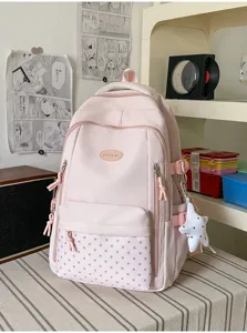 Sac à dos rose posé sur un lit rayé, avec poche avant à étoiles et breloque suspendue