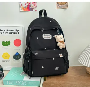 Détail d’un sac à dos noir aux cœurs et étoiles brodés, avec un ourson en peluche suspendu