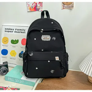 Sac à dos noir brodé, posé sur une table en bois près de livres et d’un appareil photo