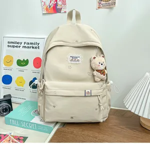 Sac à dos crème posé sur une table, avec motifs brodés, écusson en tissu et pendentif ours