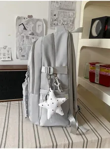 Vue latérale d’un sac gris avec compartiments zippés, boucle à sangle et pendentif étoile blanc