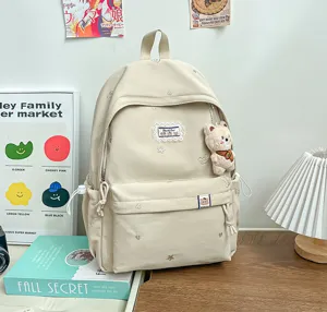 Sac à dos ivoire mat avec pendentif ourson, broderies et poche zippée, posé sur une table