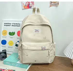Sac à dos crème posé sur un bureau, avec broderies, écusson ours, cordons et poches zippées.