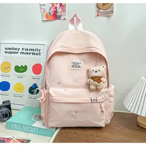 Sac à dos rose pâle vu de face, avec motifs brodés, poche zippée et petit pendentif ours