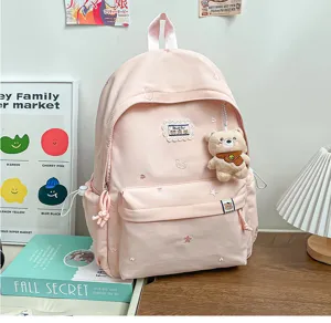 Sac à dos rose posé sur un bureau, avec livres, étoiles et cœurs brodés, et un pendentif ourson