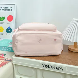 Sac à dos scolaire rose en nylon, orné de broderies et posé à plat sur une surface éclairée