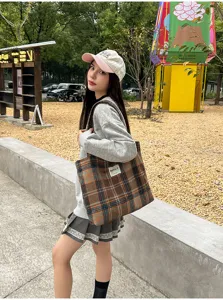 Outdoor view of a model carrying a brown-orange plaid tote with long straps and white label.