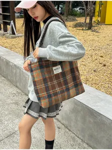 Outdoor view of a woman carrying a brown, orange and blue plaid tote bag by its handles