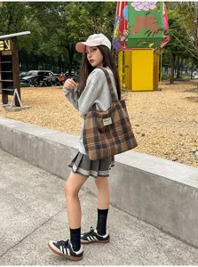 Street-style view of a model carrying a brown, orange and navy plaid tote bag outdoors