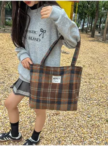 A model carries a brown plaid fabric tote by its long shoulder straps outdoors