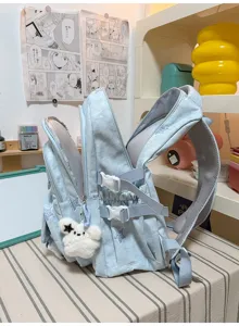 Vue de côté d’un sac à dos bleu clair, avec bretelles grises, boucles et pendentif ours en peluche