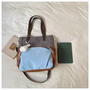 Vue à plat d’un sac gris, bleu et marron avec un pendentif lapin en peluche près d’une tablette