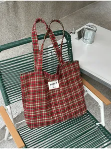 Red and green plaid fabric tote with handles, displayed on a green metal chair in a casual setting