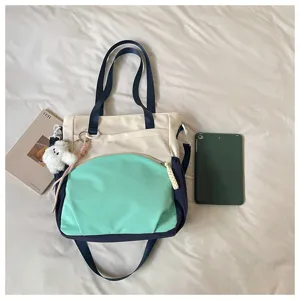 Vue à plat du sac vert menthe, crème et bleu marine, avec poche zippée et porte-clés en peluche