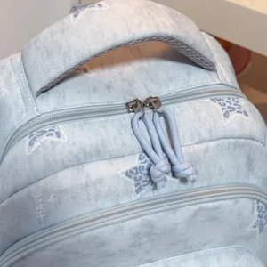Sac à dos bleu clair délavé, motifs imprimés et tirettes assorties, photographié de près en biais