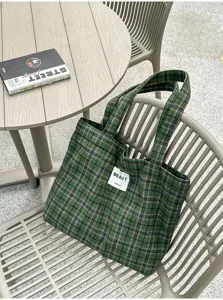 Green plaid tote with woven fabric, double handles and stitched label, shown on a chair