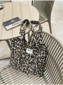 Close-up of a plush leopard-print bag with twin handles and a front label on a chair