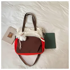 Vue à plat d’un sac en nylon avec poche zippée, deux anses et un pendentif blanc en peluche