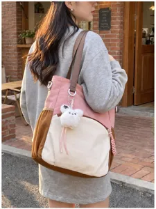Une femme porte devant un café un sac rose, crème et caramel avec un pendentif ourson en peluche